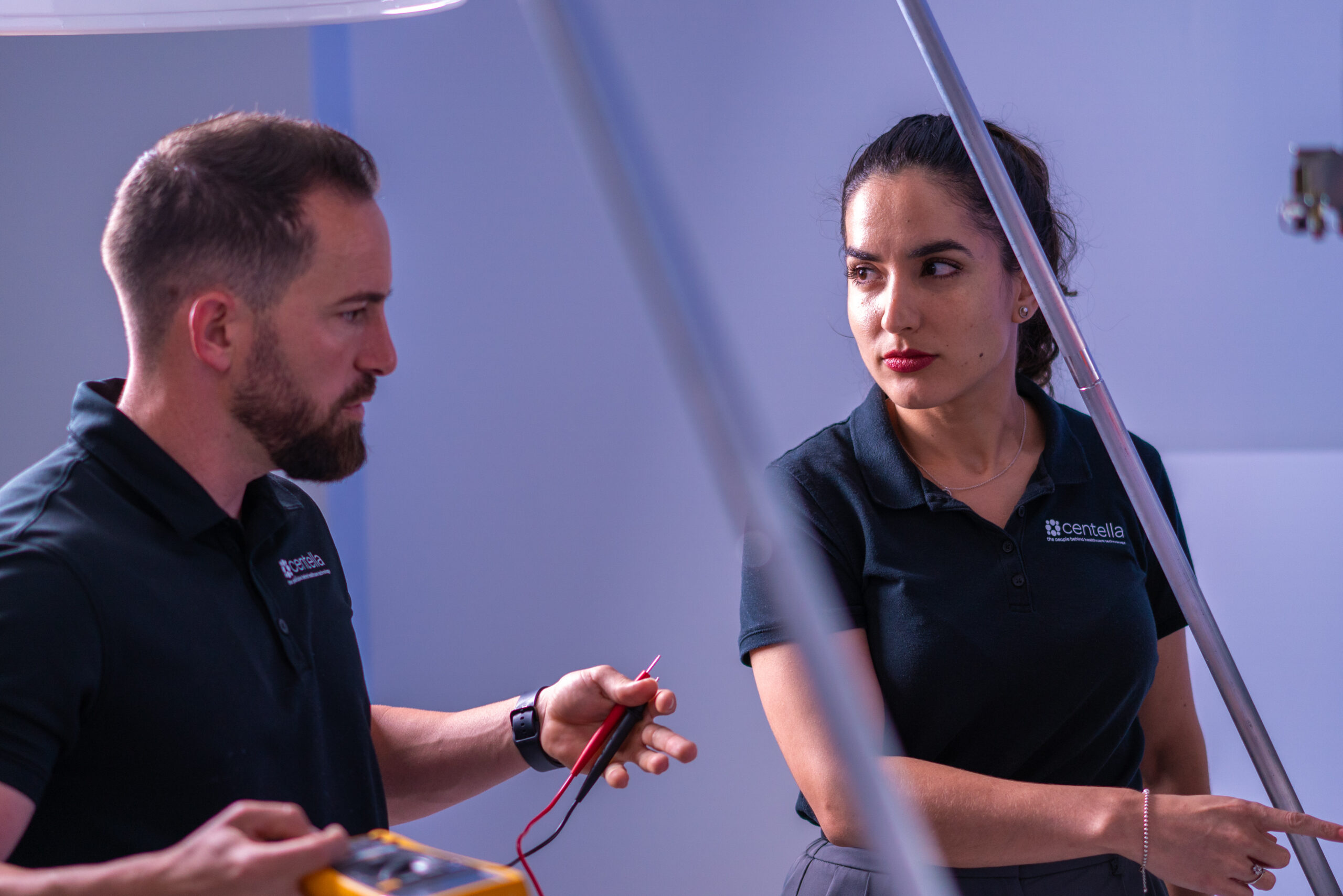 Two Centella technicians using a multimeter to test MRI equipment during a service visit